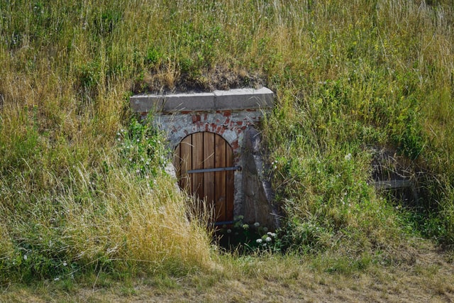 fotografía de una entrada con la puerta de madera y enclavada en la ladera de una montaña cubierta de vegetación