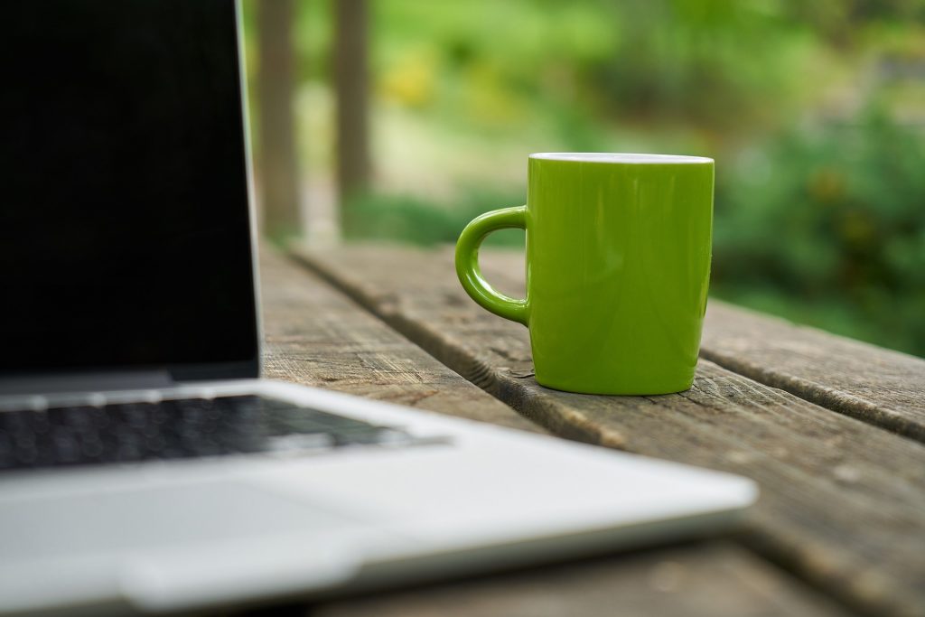 Imagen en primer plano de una taza verde al lado de un ordenador portátil